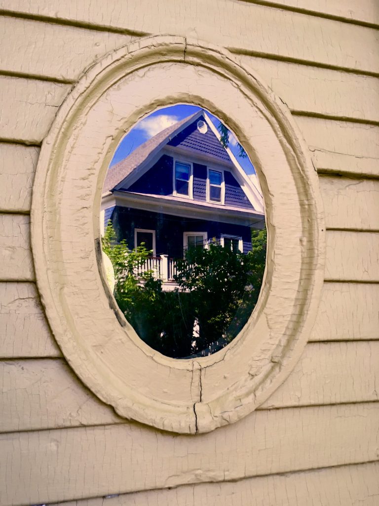 Circular window with house reflected in the glass.